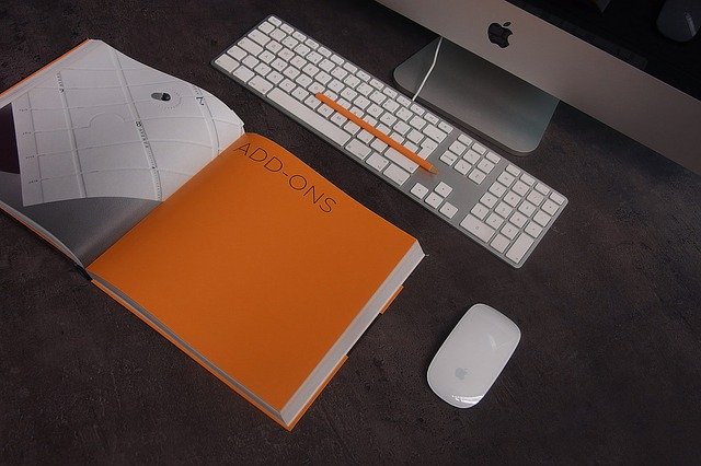 Otvorená kniha s oranžovou stranou, klávesnica a počítač